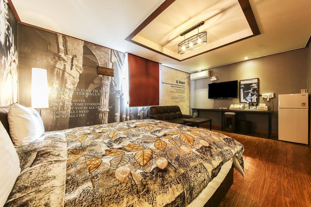 A hotel room with a bed, a desk, a television, and a refrigerator.