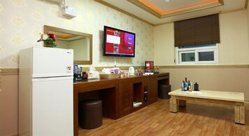 Un baño de hotel con tocador de madera, refrigerador, televisor y ventana con persianas.