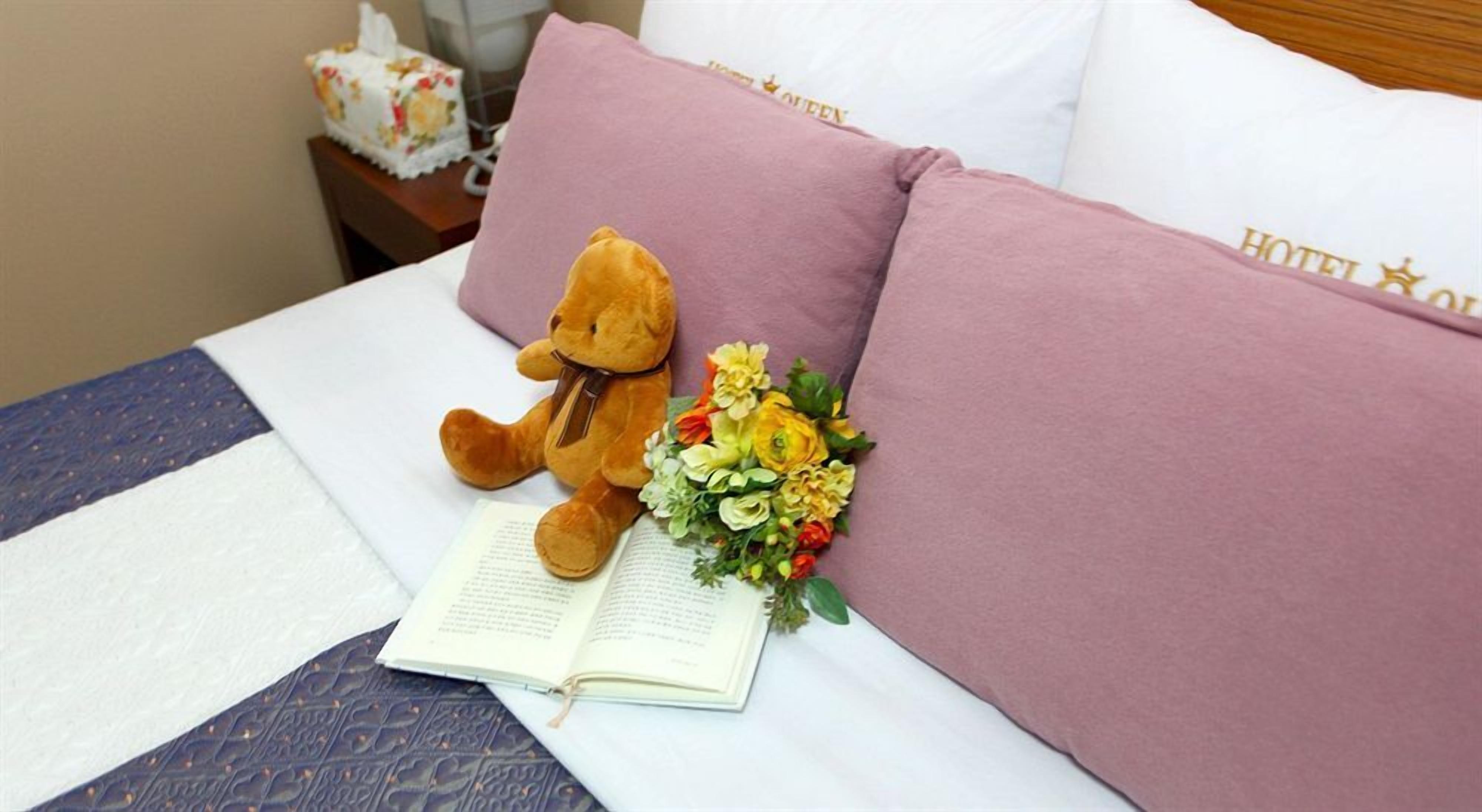 A bed with a teddy bear, a bouquet of flowers, and a book.