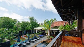 A pool area with lounge chairs and umbrellas, surrounded by greenery and a building with a tiled roof. - GZ Eden Privilege Resort and Spa (Siem Reap)