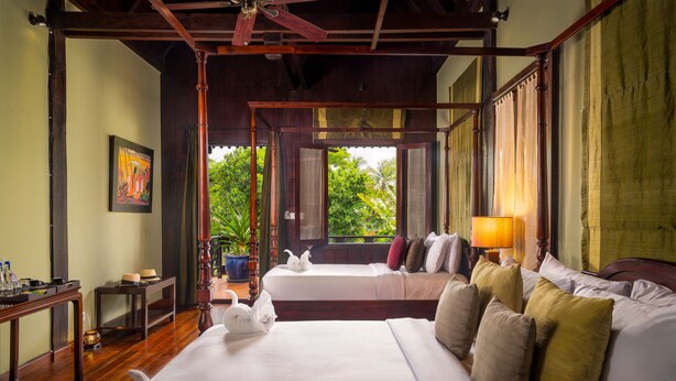 A spacious bedroom with a large bed, a wooden ceiling, a window with a view of greenery, and a bedside table with a lamp. - GZ Eden Privilege Resort and Spa (Siem Reap)
