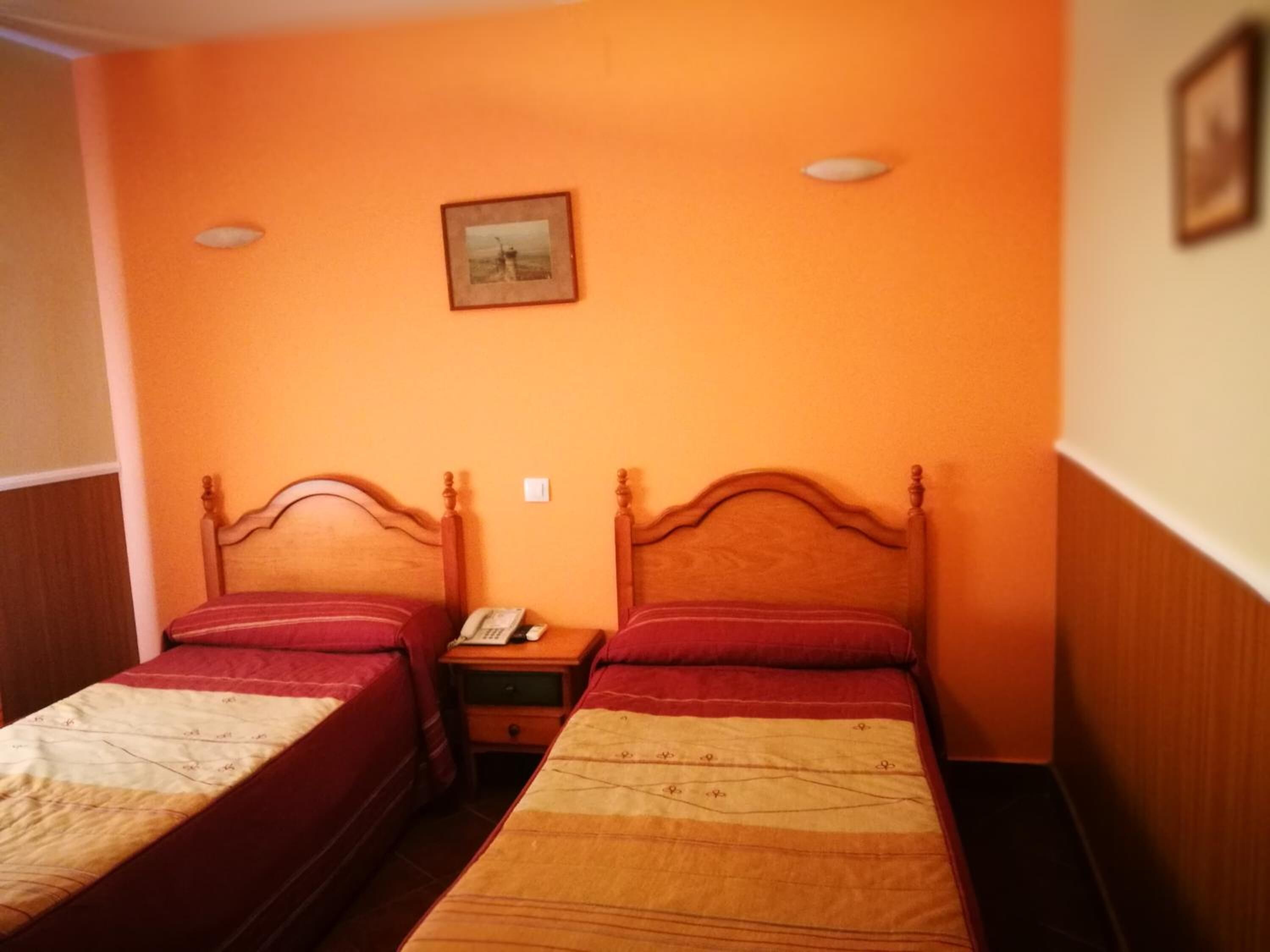 A room with two single beds, wooden headboards, and a small bedside table with a phone.