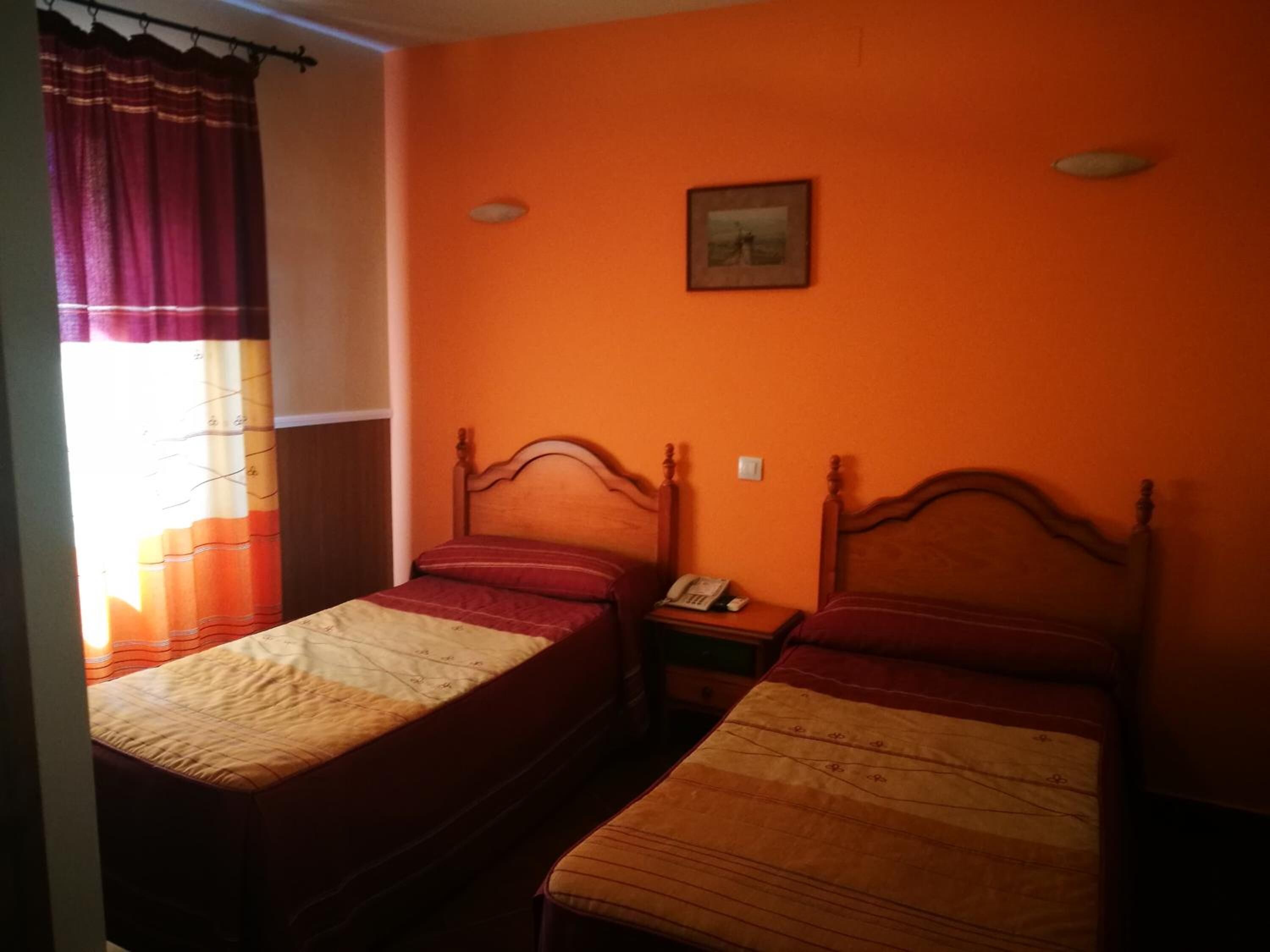 A room with two single beds, a nightstand with a telephone, and a window with curtains.