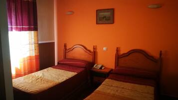 A room with two single beds, a nightstand with a telephone, and a window with curtains.