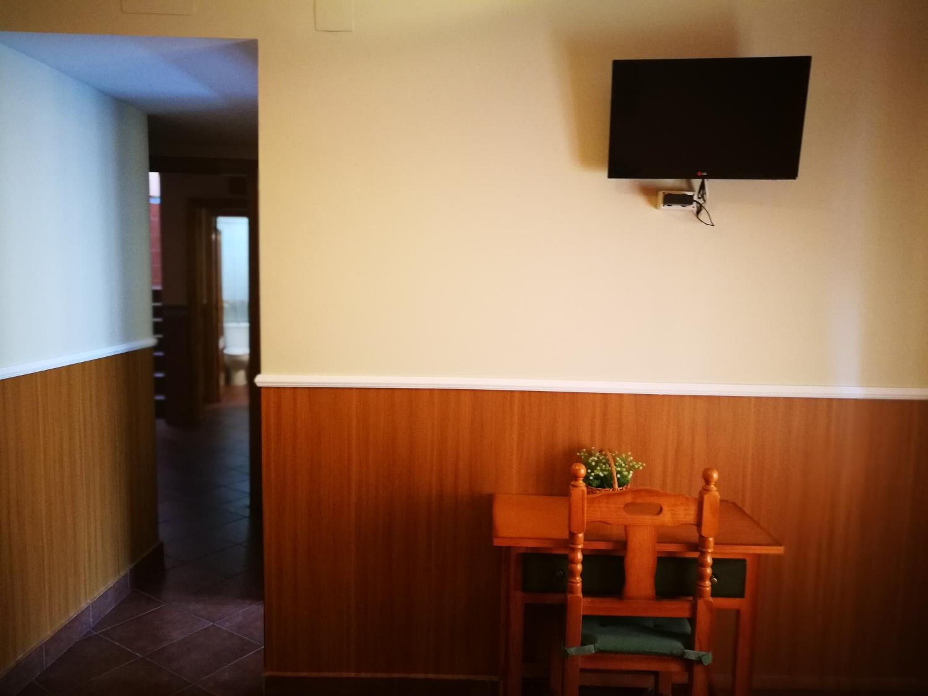 A hotel room with a wooden panel wall, a flat-screen TV mounted on the wall, and a wooden table with a chair.