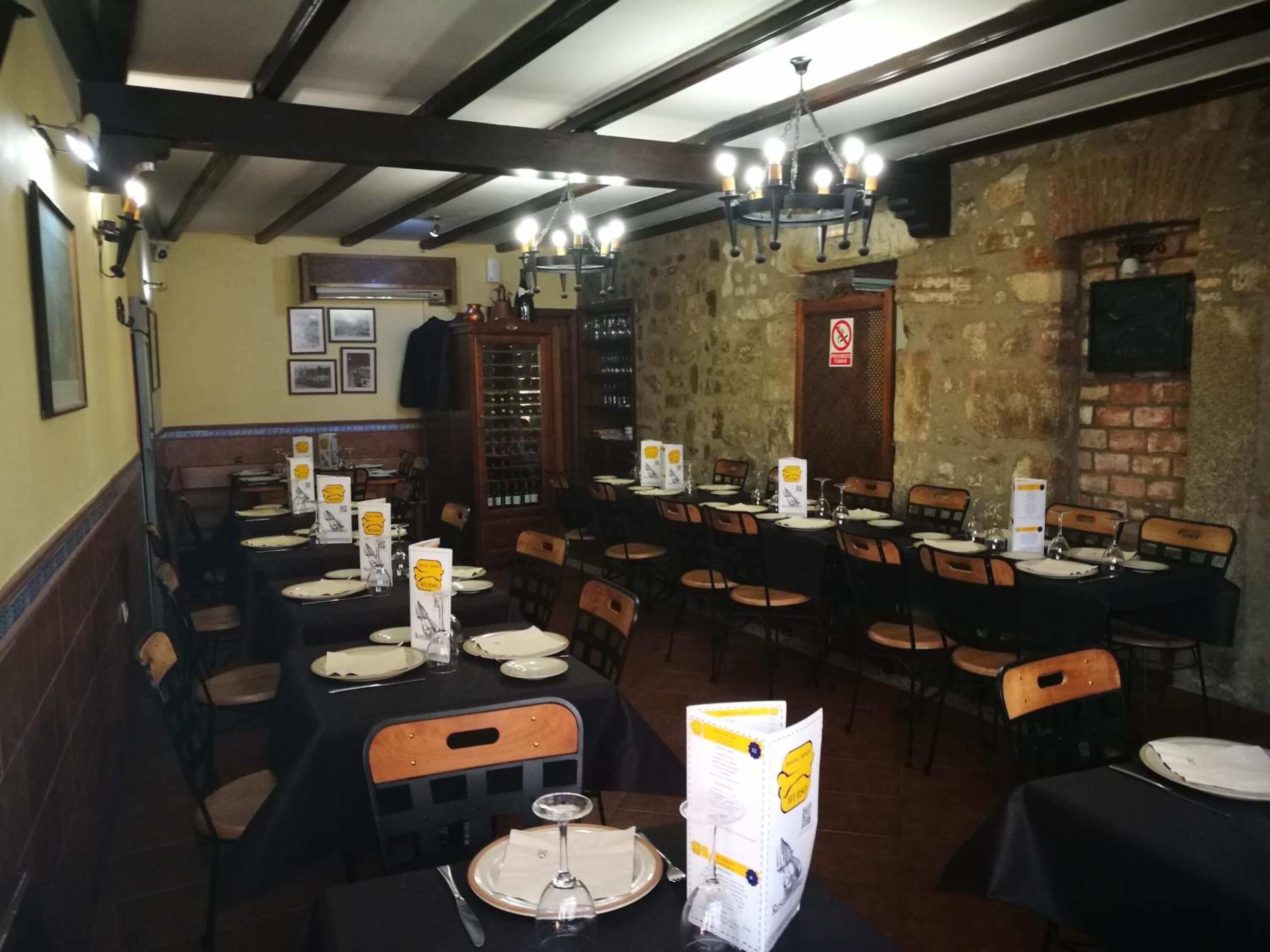 Un restaurante con varias mesas dispuestas para comer, con manteles negros, sillas de madera y un candelabro.
