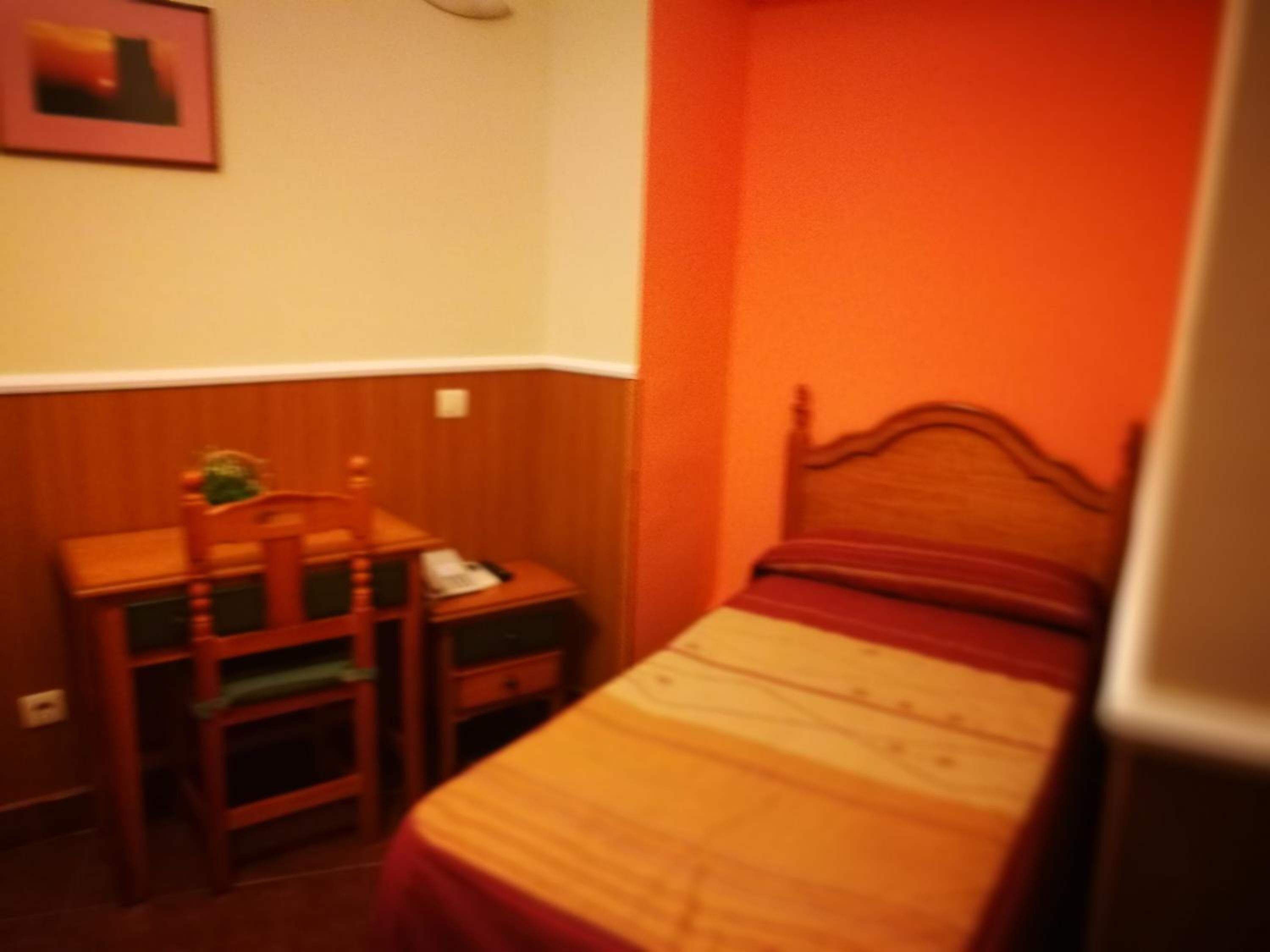 Une petite pièce avec un lit, un bureau en bois et une chaise.