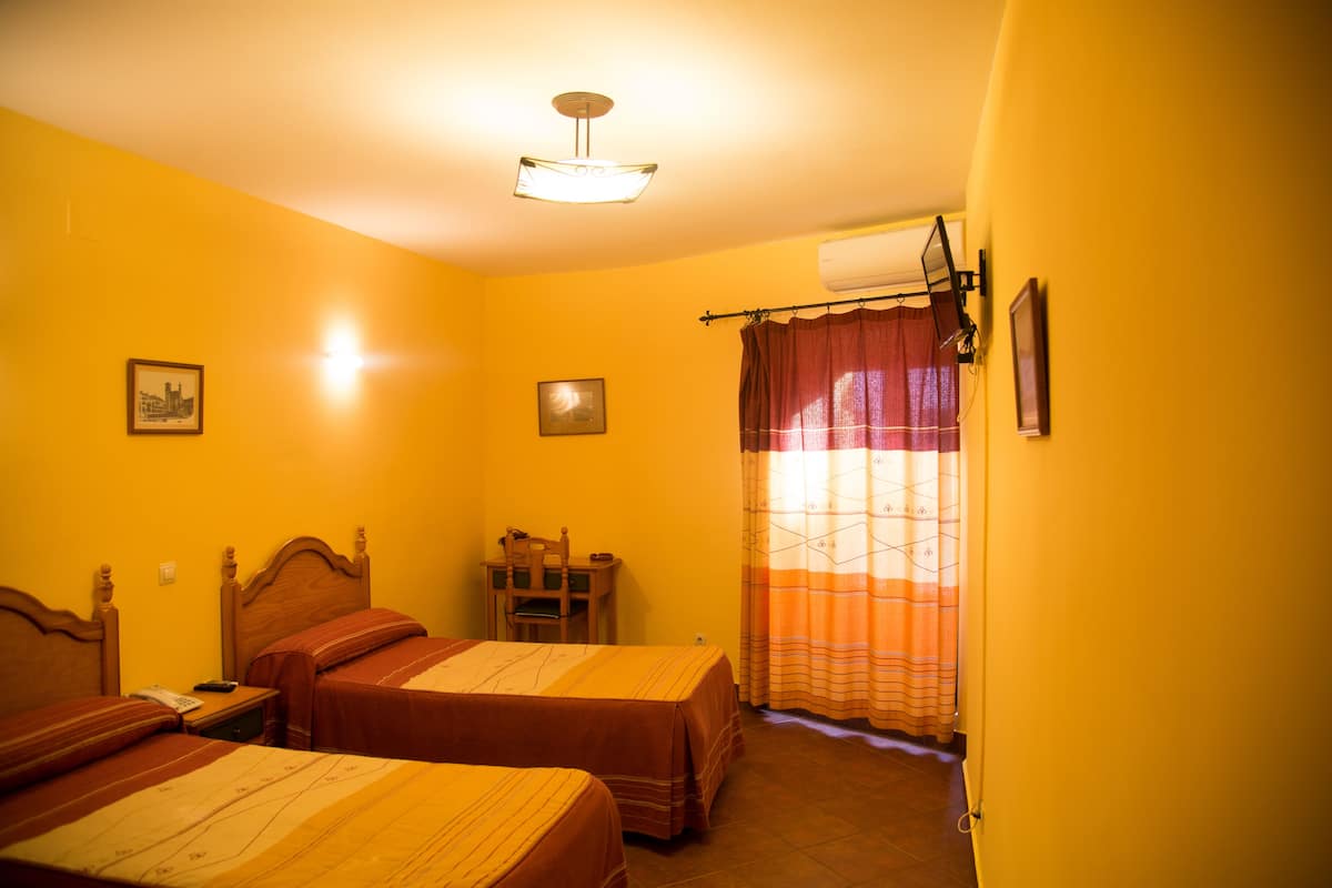 Una habitación de hotel con dos camas, una mesita de noche de madera, una pequeña mesa y una lámpara en el techo.