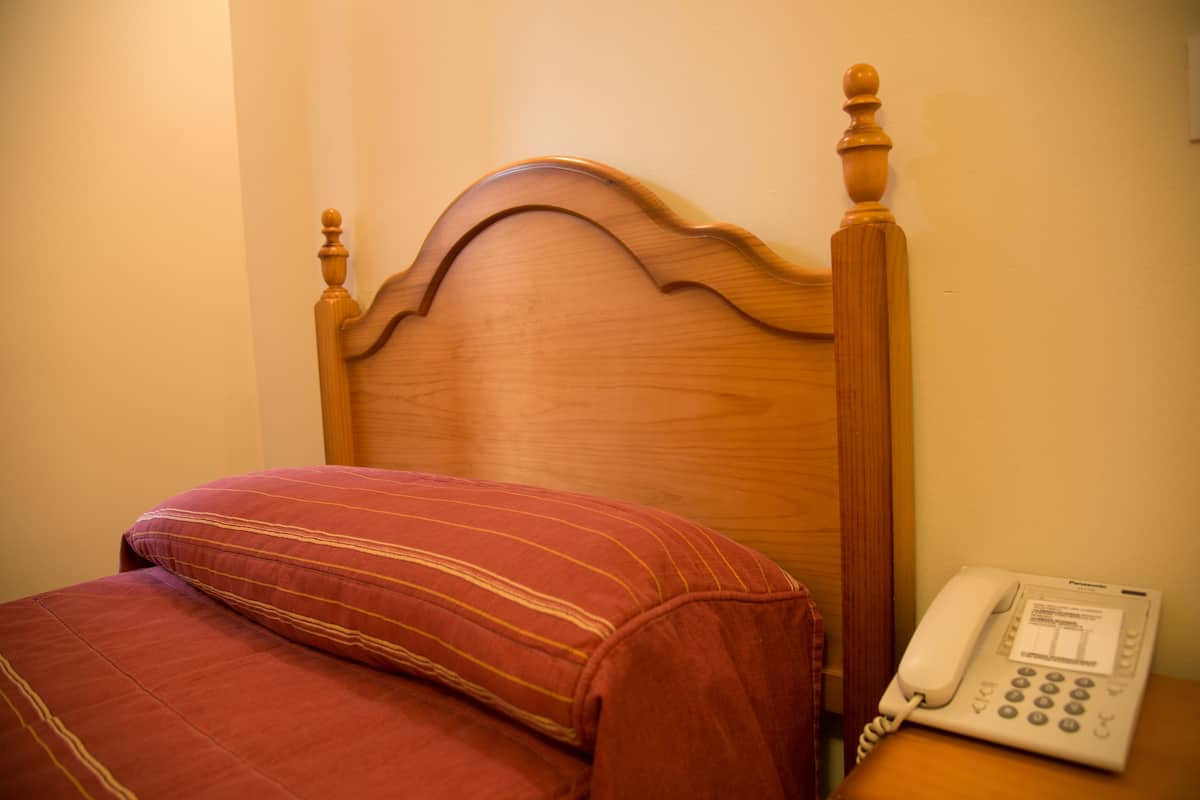 Una cama de madera con un cojín rojo a rayas y un teléfono blanco en la mesita de noche.