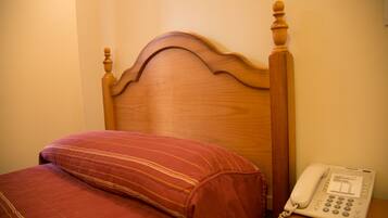 A wooden bed with a red-striped pillow and a white bedside phone.