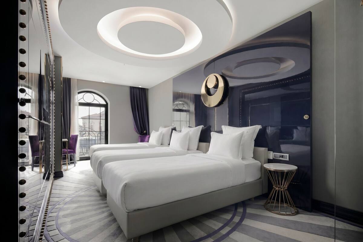 Une chambre d’hôtel moderne avec un grand lit, une petite table ronde et un miroir avec éclairage intégré.
