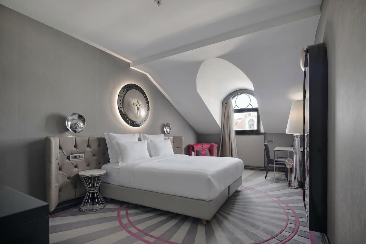 Une chambre d’hôtel moderne avec un grand lit, un miroir rond, une petite table d’appoint et un bureau avec une chaise.