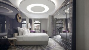 A modern hotel room with a large bed, a round ceiling light, a mirror with bead trim, and a view of the city through large windows. - Sura Design Hotel and Suites - Boutique Class (Istanbul)