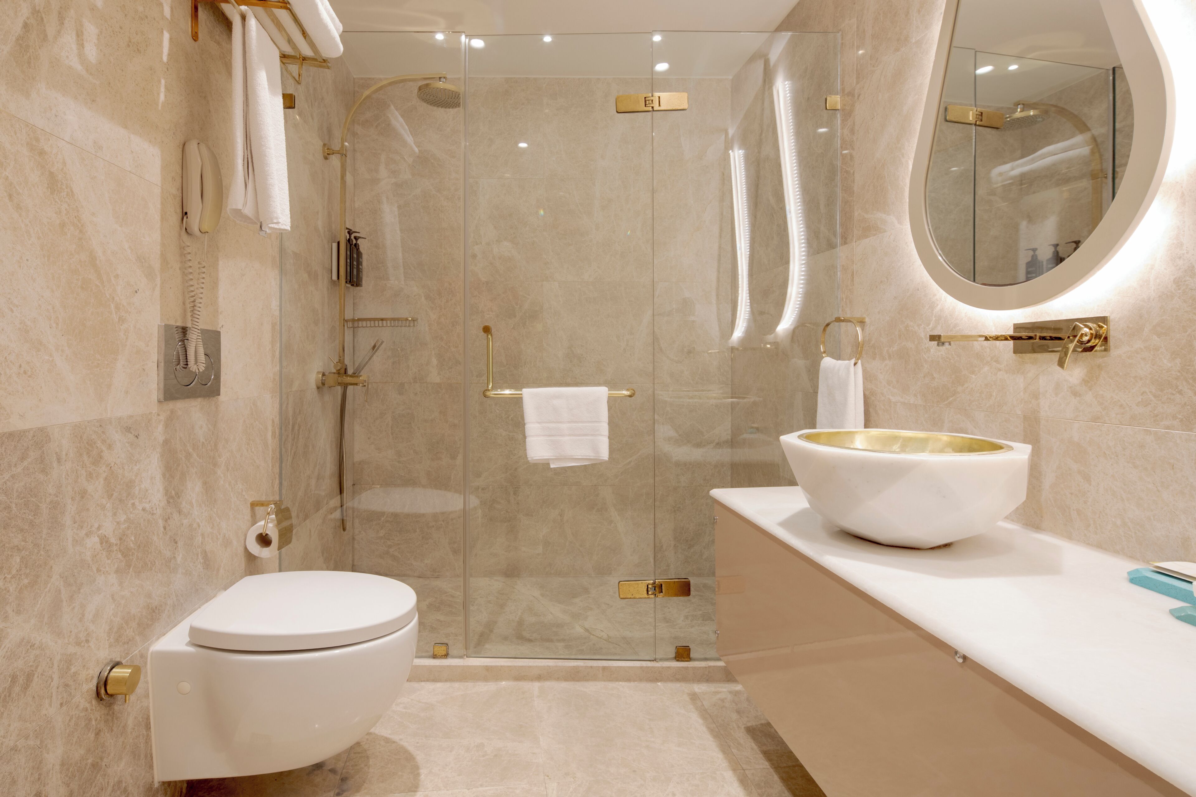 Et moderne badeværelse med et glasafskærmet brusebad, et hvidt toilet og et stort, ovalt spejl.