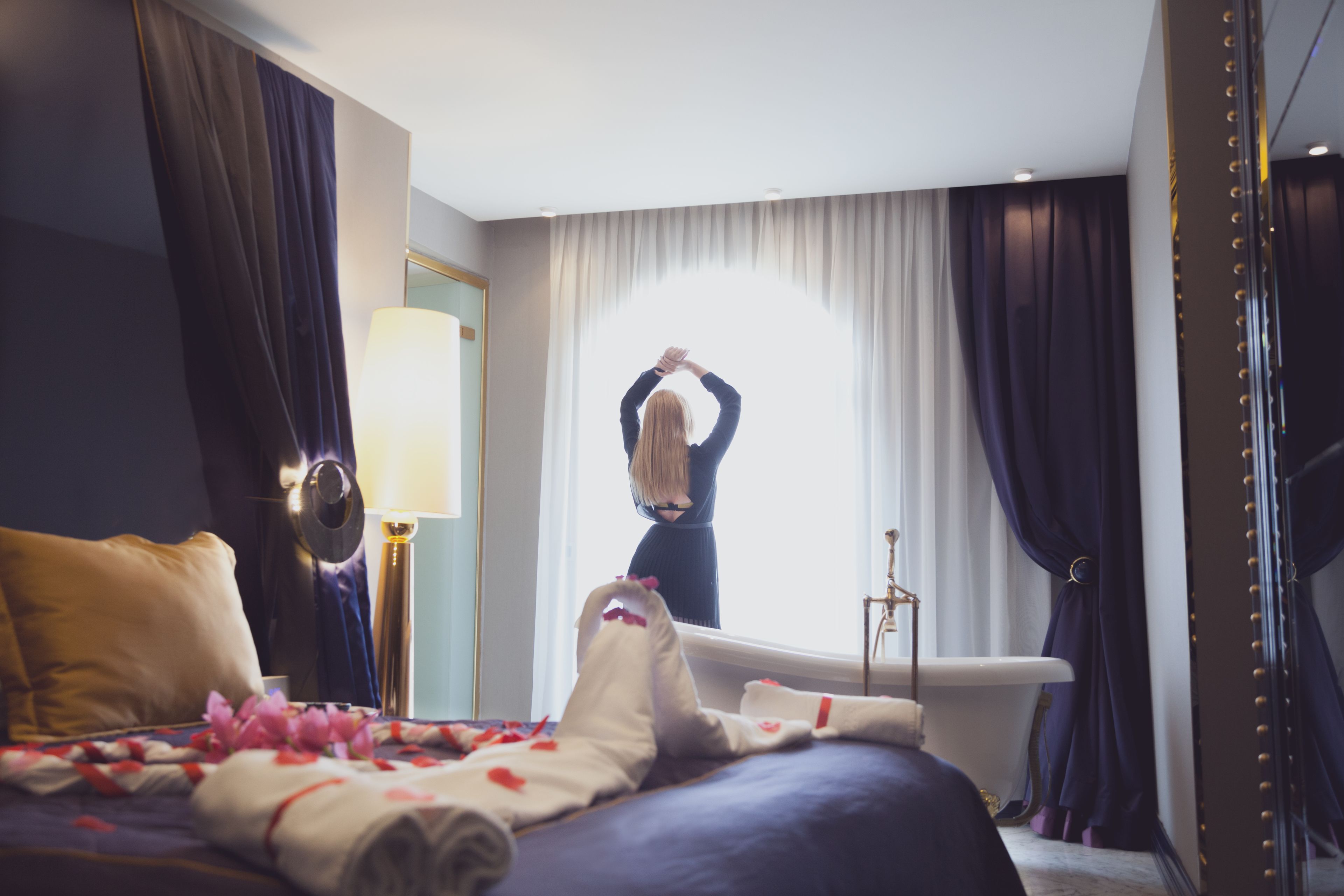 Una habitación de hotel con cama, bañera y un amplio ventanal con cortinas.