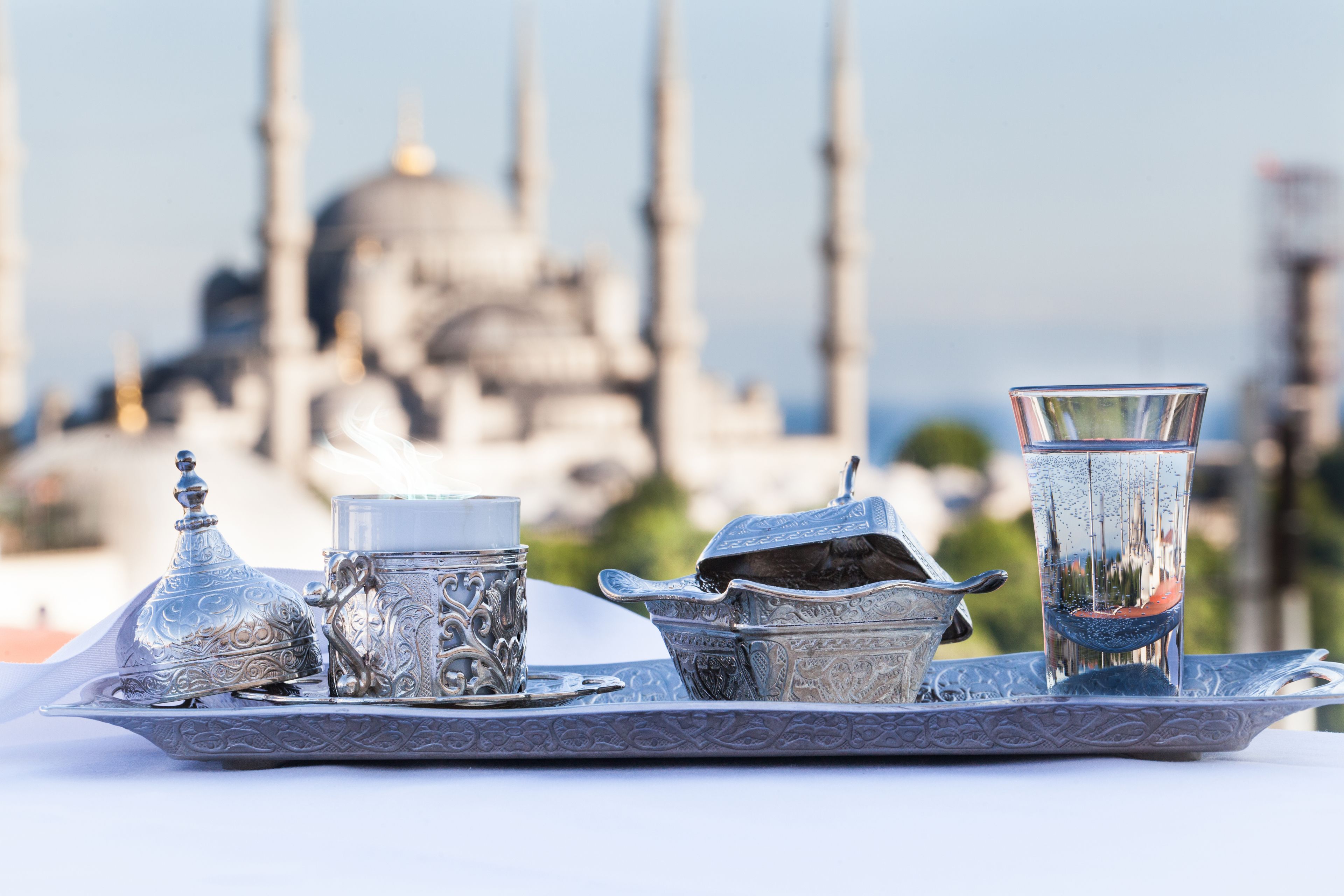 Un vassoio con teiera, tazza e bicchiere, sullo sfondo una moschea.