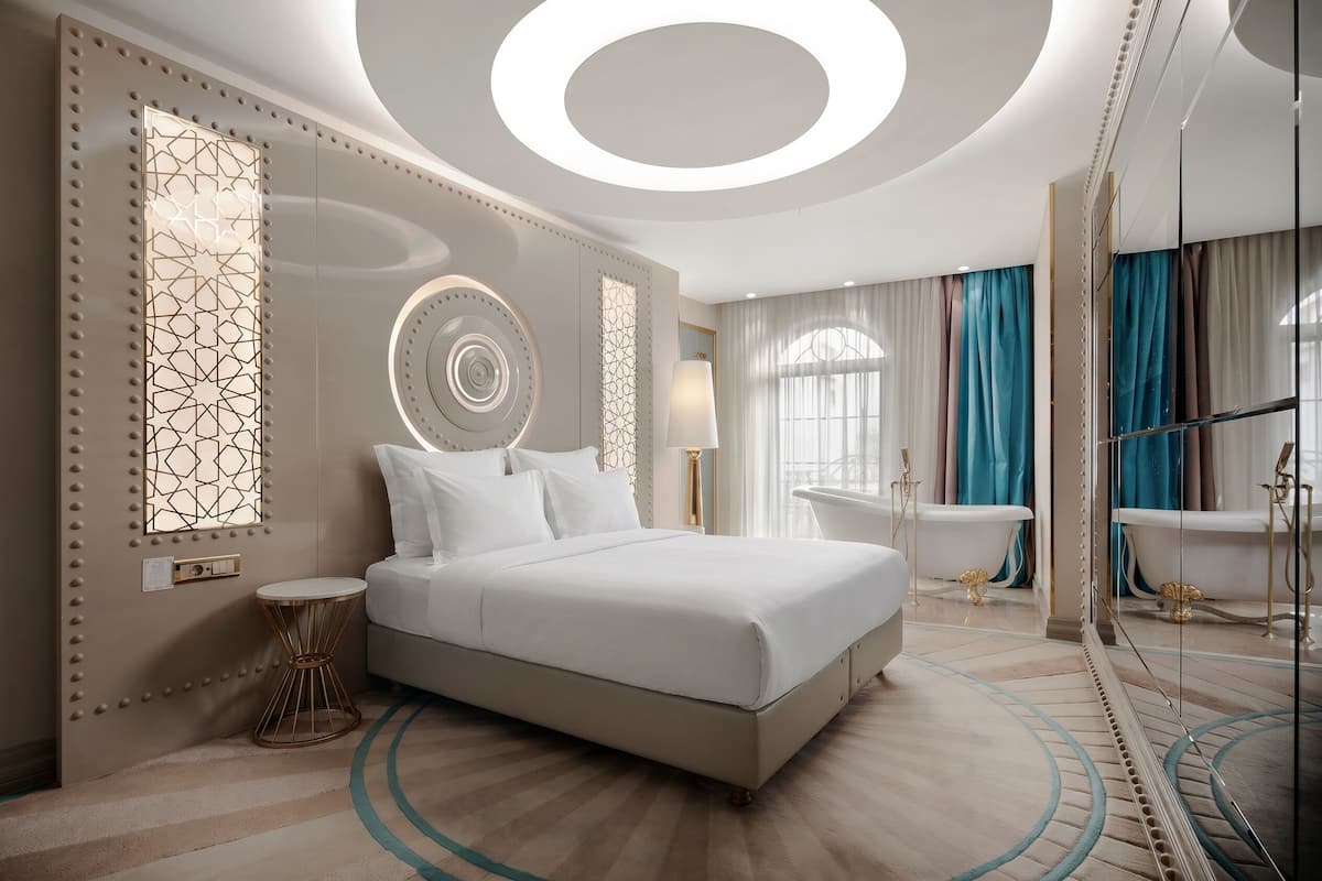 Une chambre d’hôtel moderne avec un grand lit, un miroir rond, une baignoire et une coiffeuse avec un miroir.