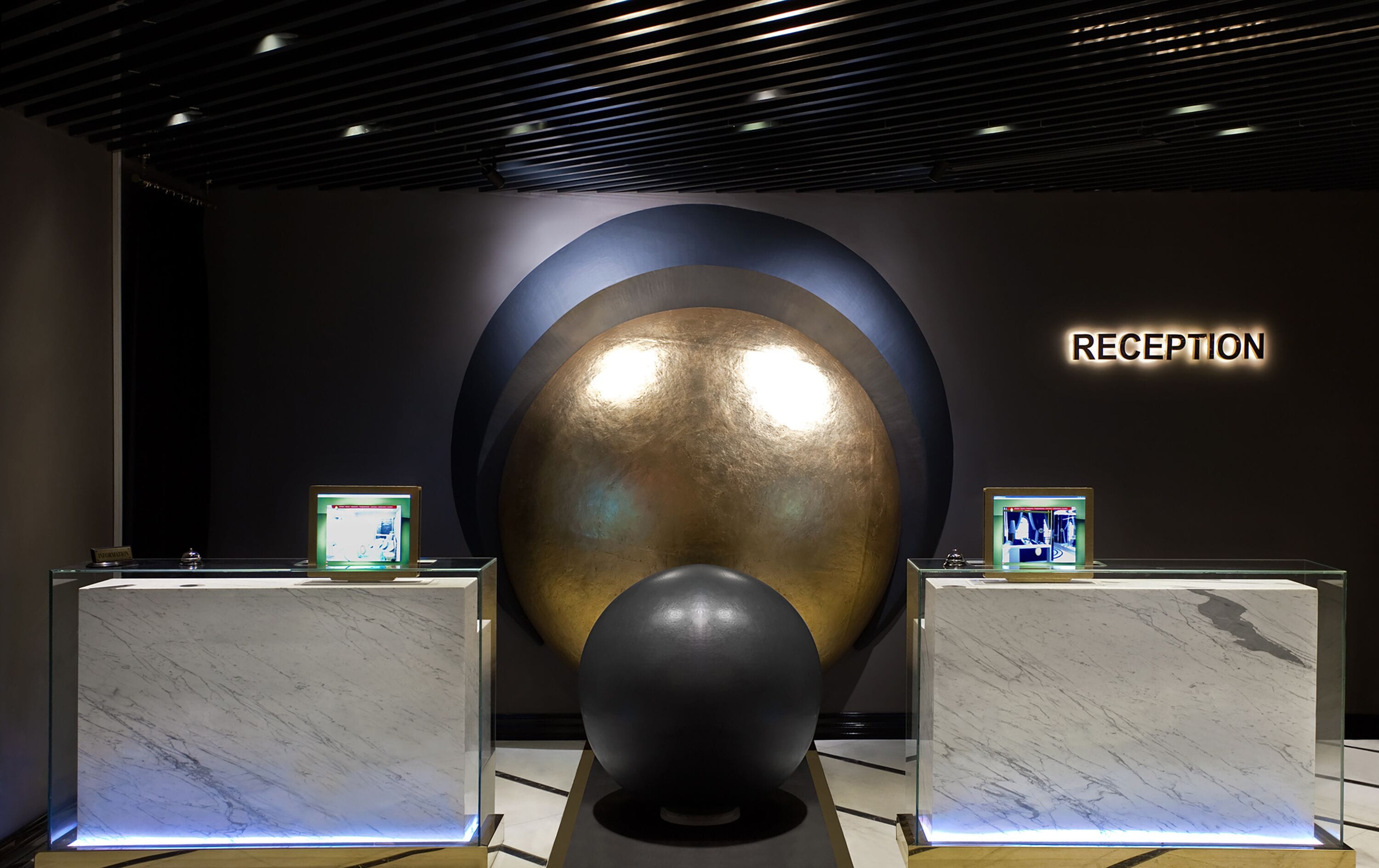 Un espace d’accueil comprenant une grande sculpture sphérique, deux vitrines et une enseigne indiquant « RÉCEPTION ».