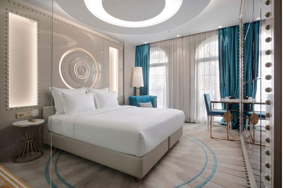 Une chambre d’hôtel moderne dotée d’un grand lit, d’une coiffeuse avec des miroirs et d’un coin salon comprenant une table et des chaises.
