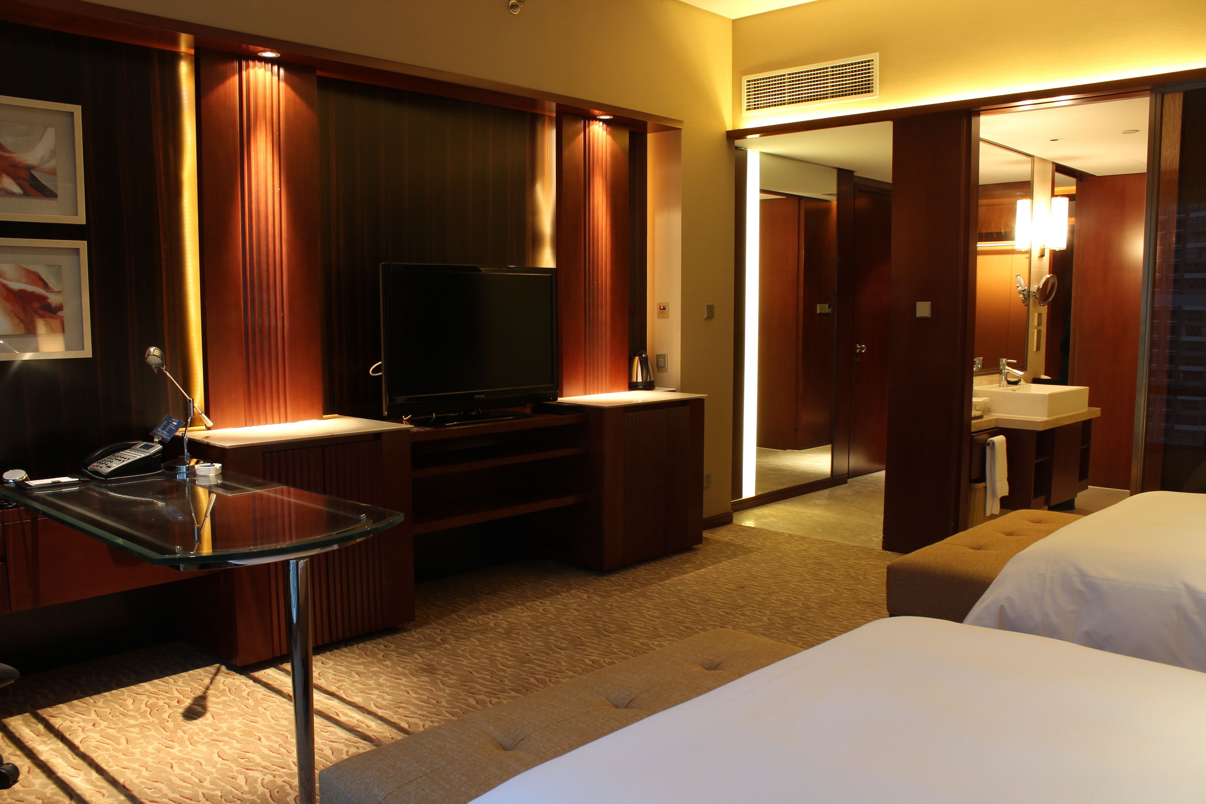 Habitación de hotel con escritorio de vidrio, televisor, sofá y dos camas.