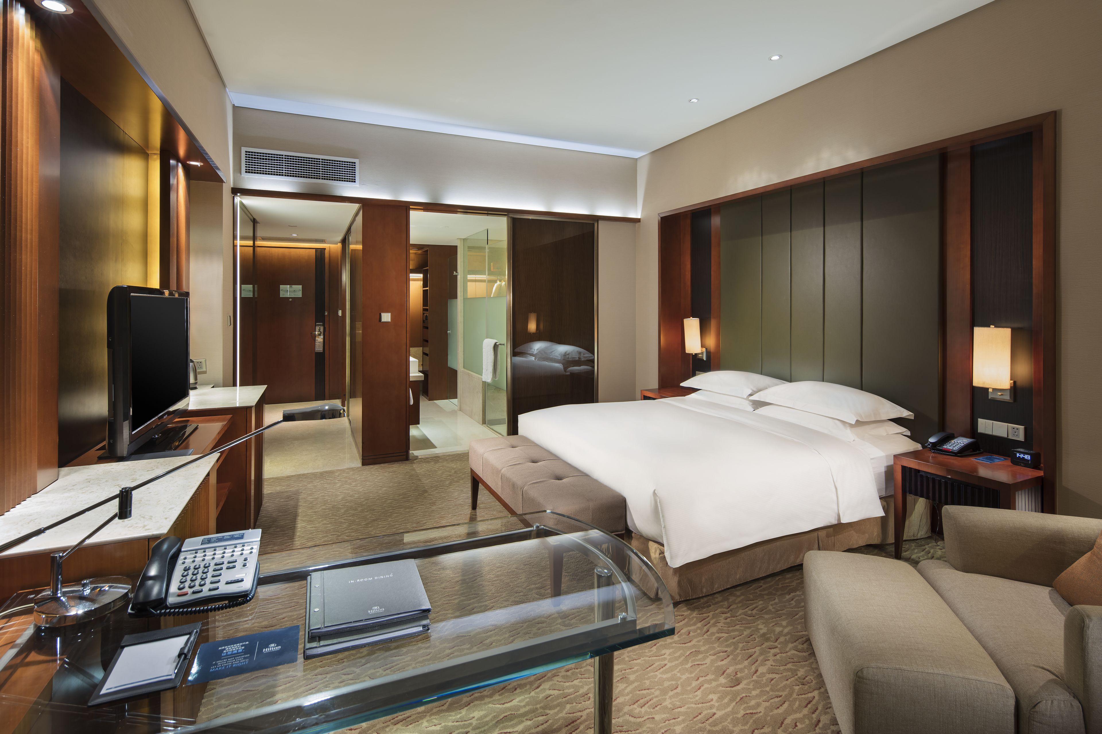 A hotel room with a large bed, a desk with a telephone and a laptop, a glass coffee table, and a seating area with a sofa.