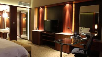 A hotel room with a bed, a glass desk, a television, and a bathroom.