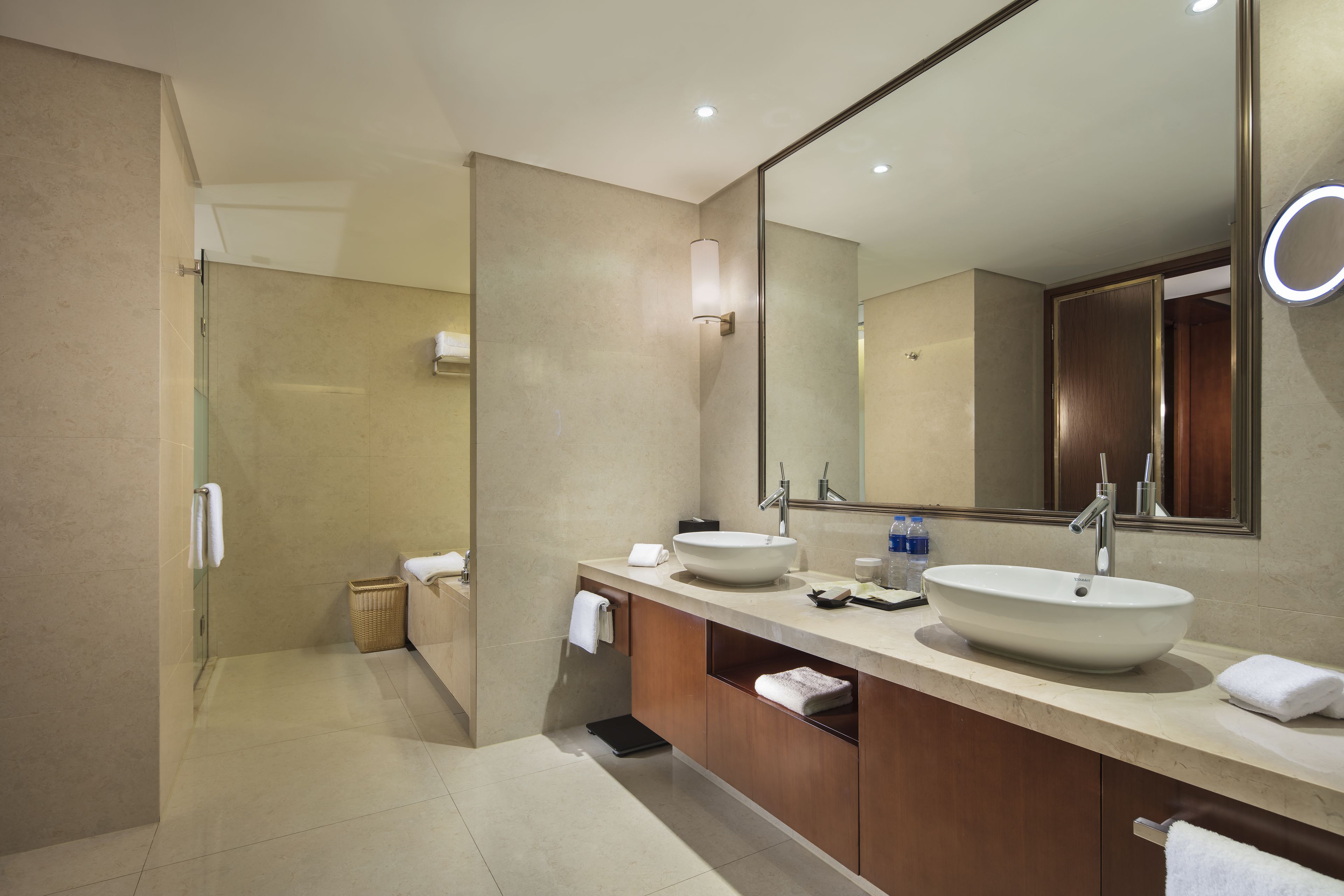 A modern bathroom with a large mirror, two sinks, and a shower area.