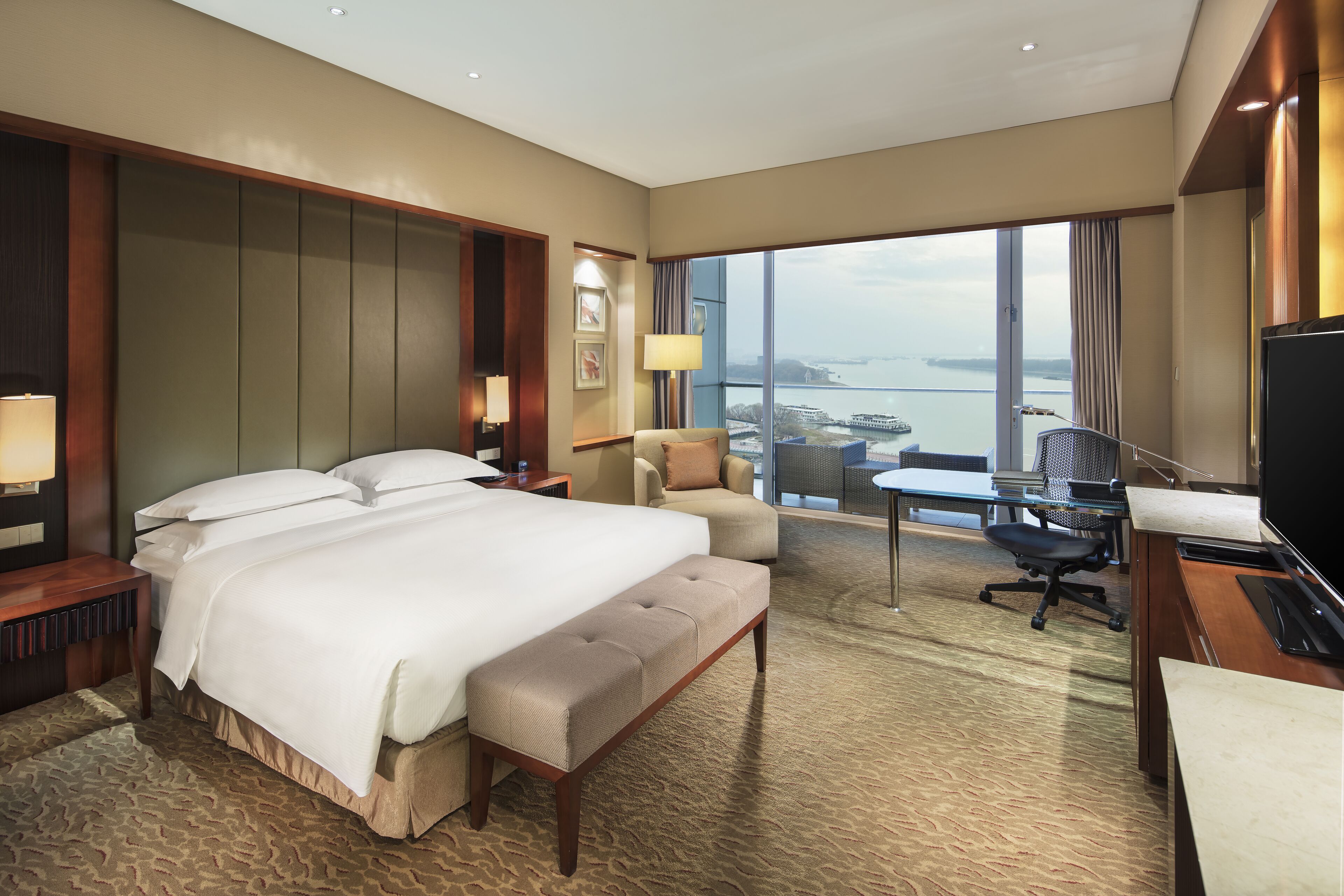 A hotel room with a large bed, a desk, a chair, and a view of the water.