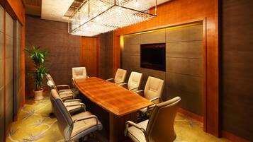 Una sala de conferencias con una mesa de madera, sillas color beige, una planta en maceta y una gran lámpara de araña.
