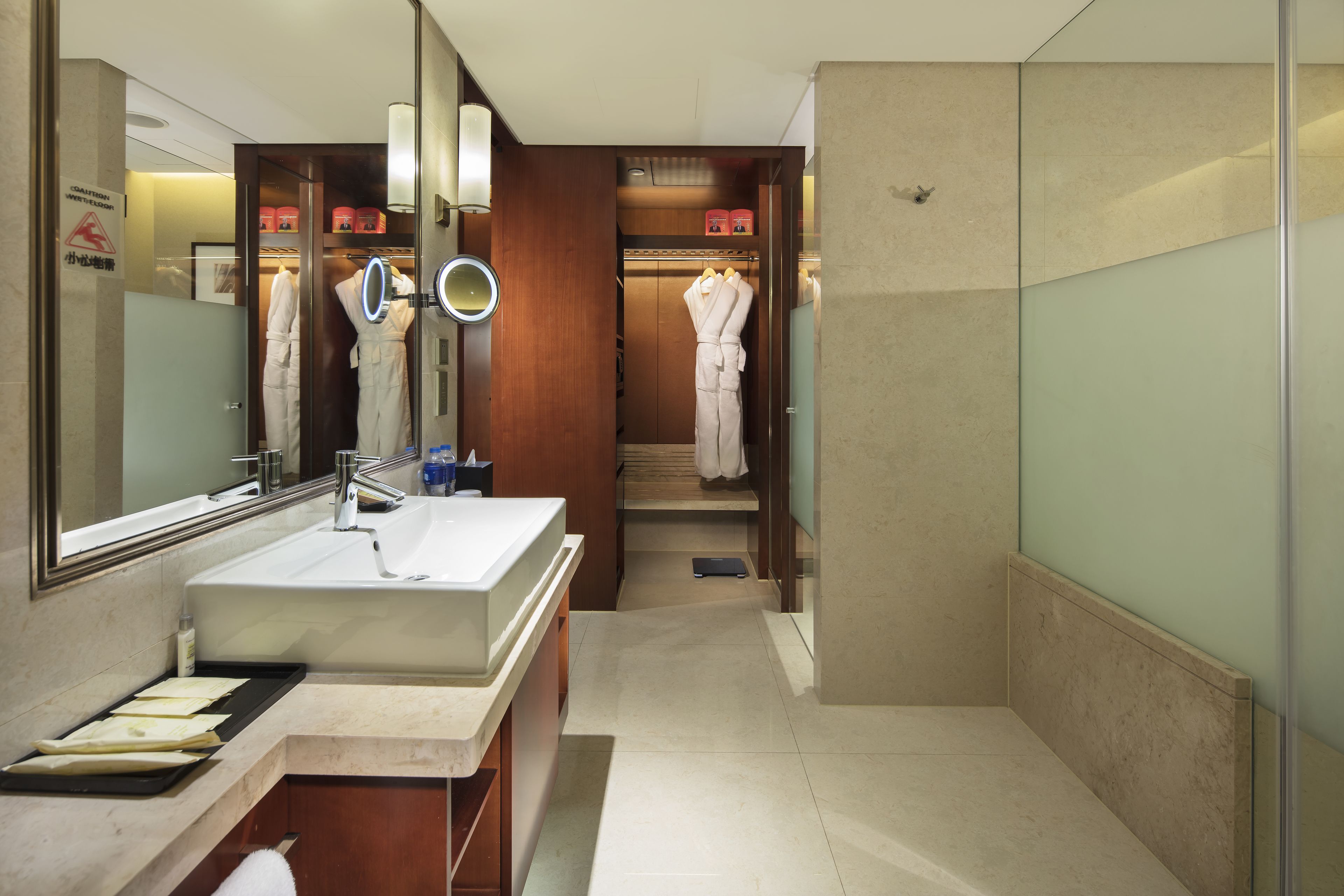 A modern bathroom with a large mirror, a sink, and a vanity. There are robes hanging in the shower area and a towel rack.