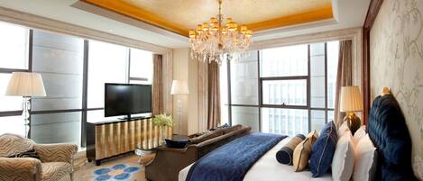 A spacious hotel room with a large bed, a television, a sofa, and a chandelier.