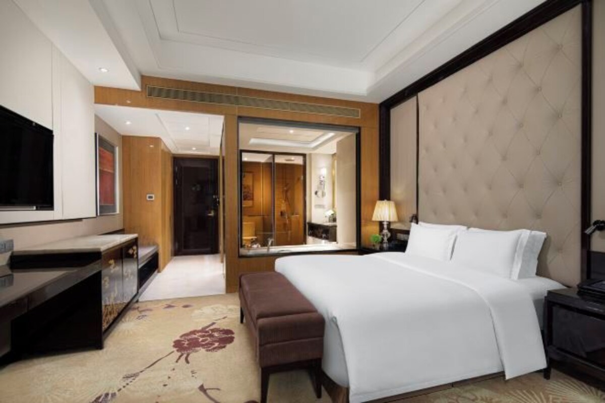 Una habitación de hotel con una cama grande, un escritorio, un televisor y un espejo.