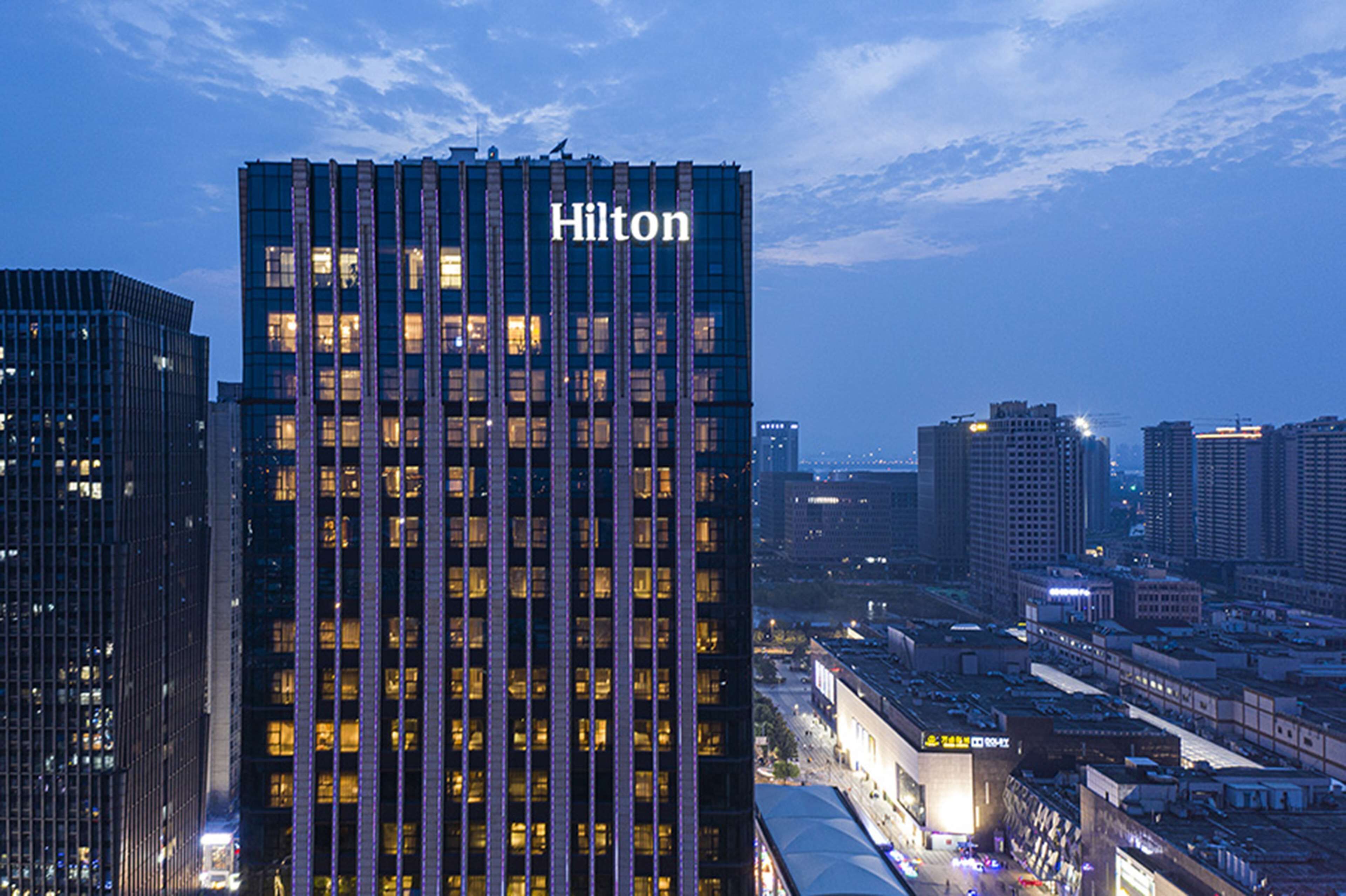 A high-rise hotel with a prominent "Hilton" sign, surrounded by other buildings and a cityscape at dusk.