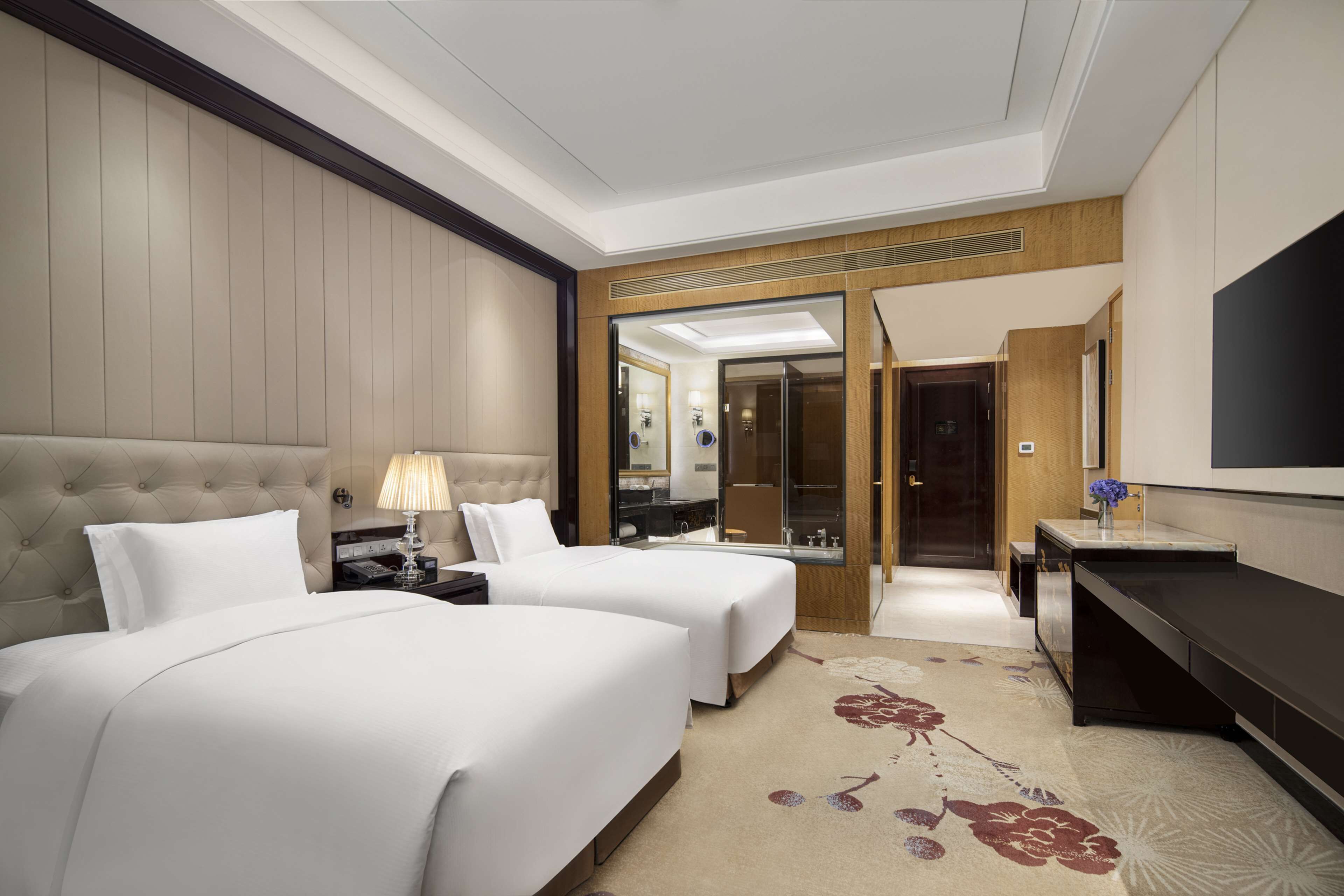 A hotel room with two beds, a TV, a desk, and a bathroom visible through an open door.