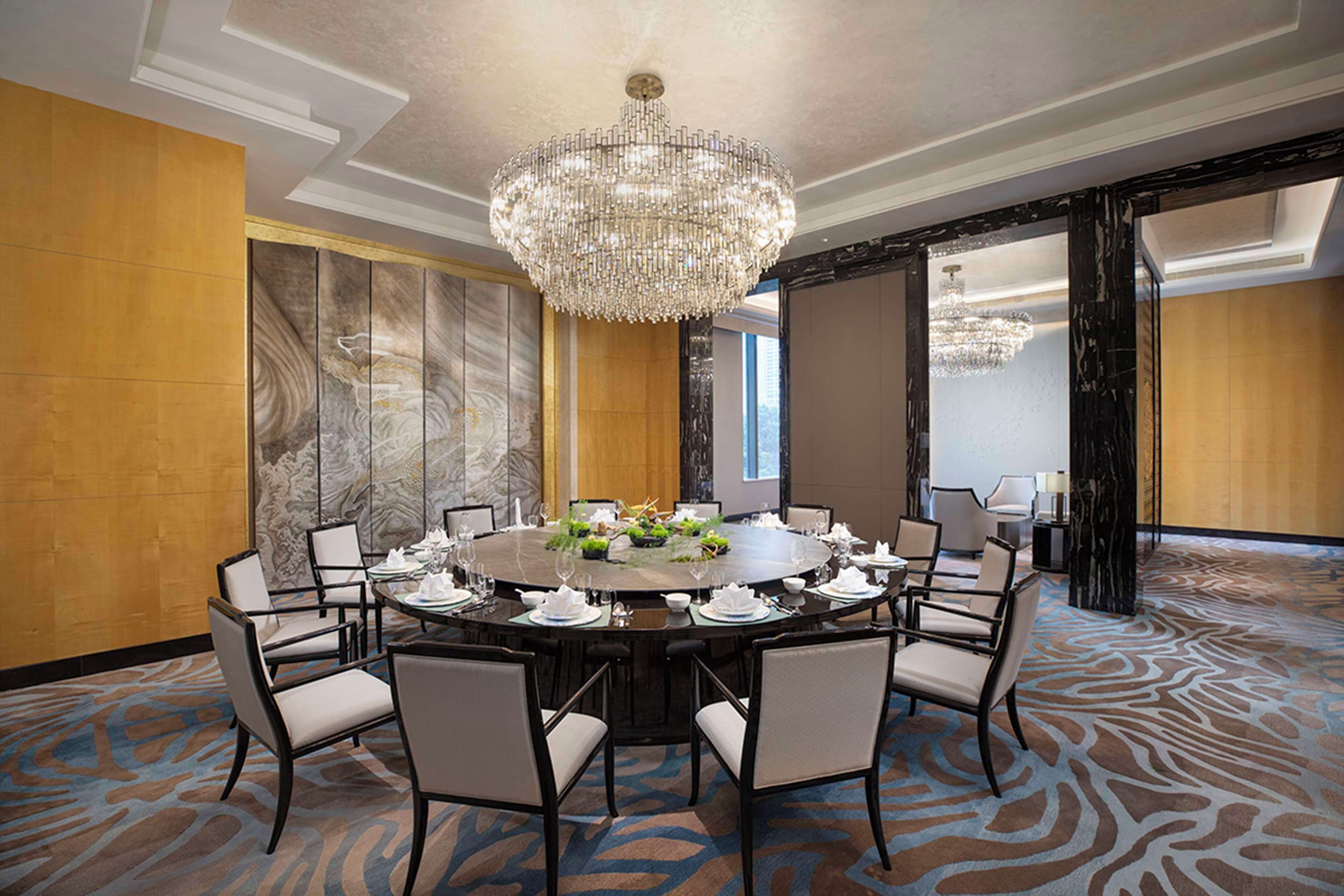 A conference room with a round table, chairs, a chandelier, and a patterned carpet.