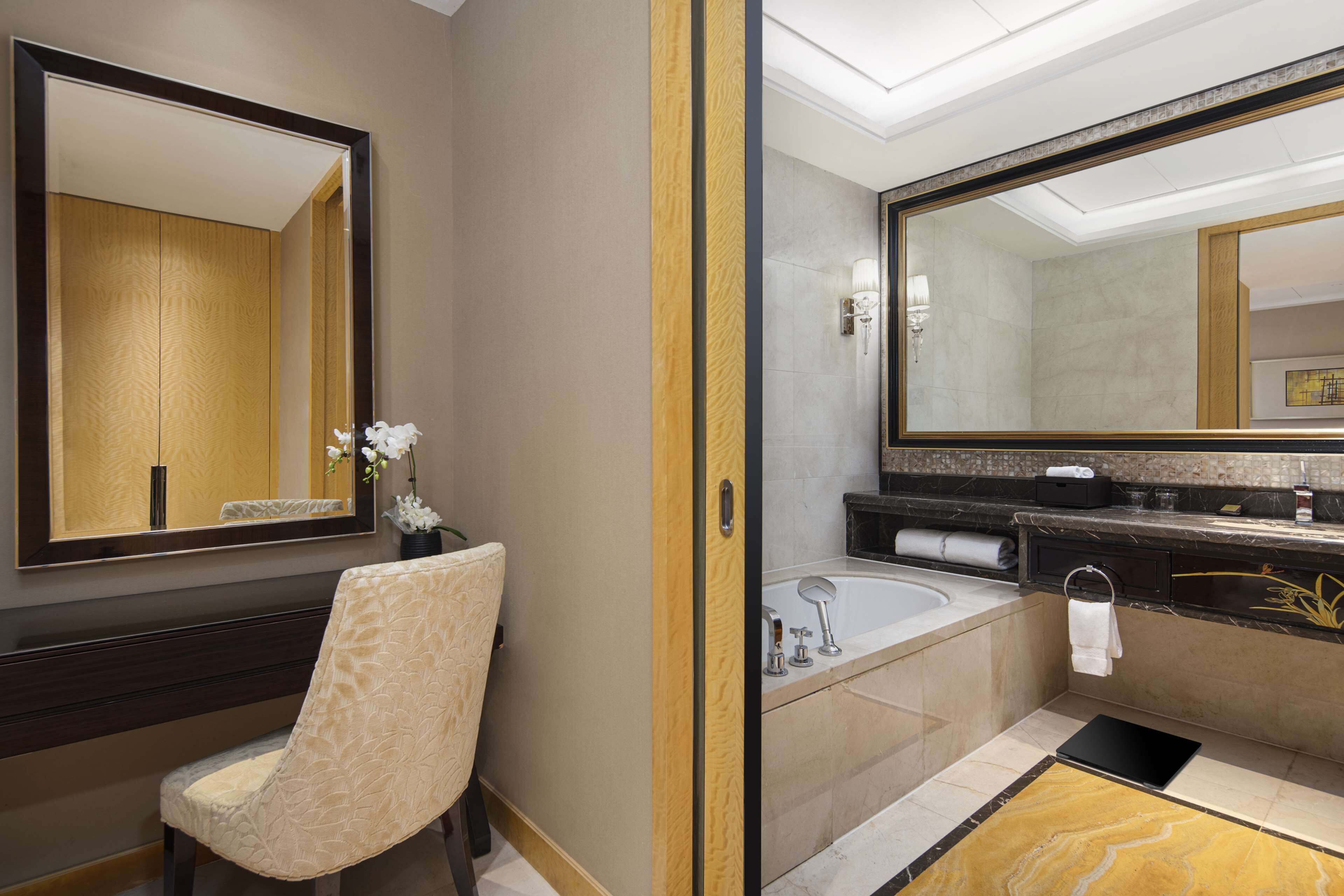 A modern bathroom with a large mirror, a bathtub, a vanity with a sink, and a chair.