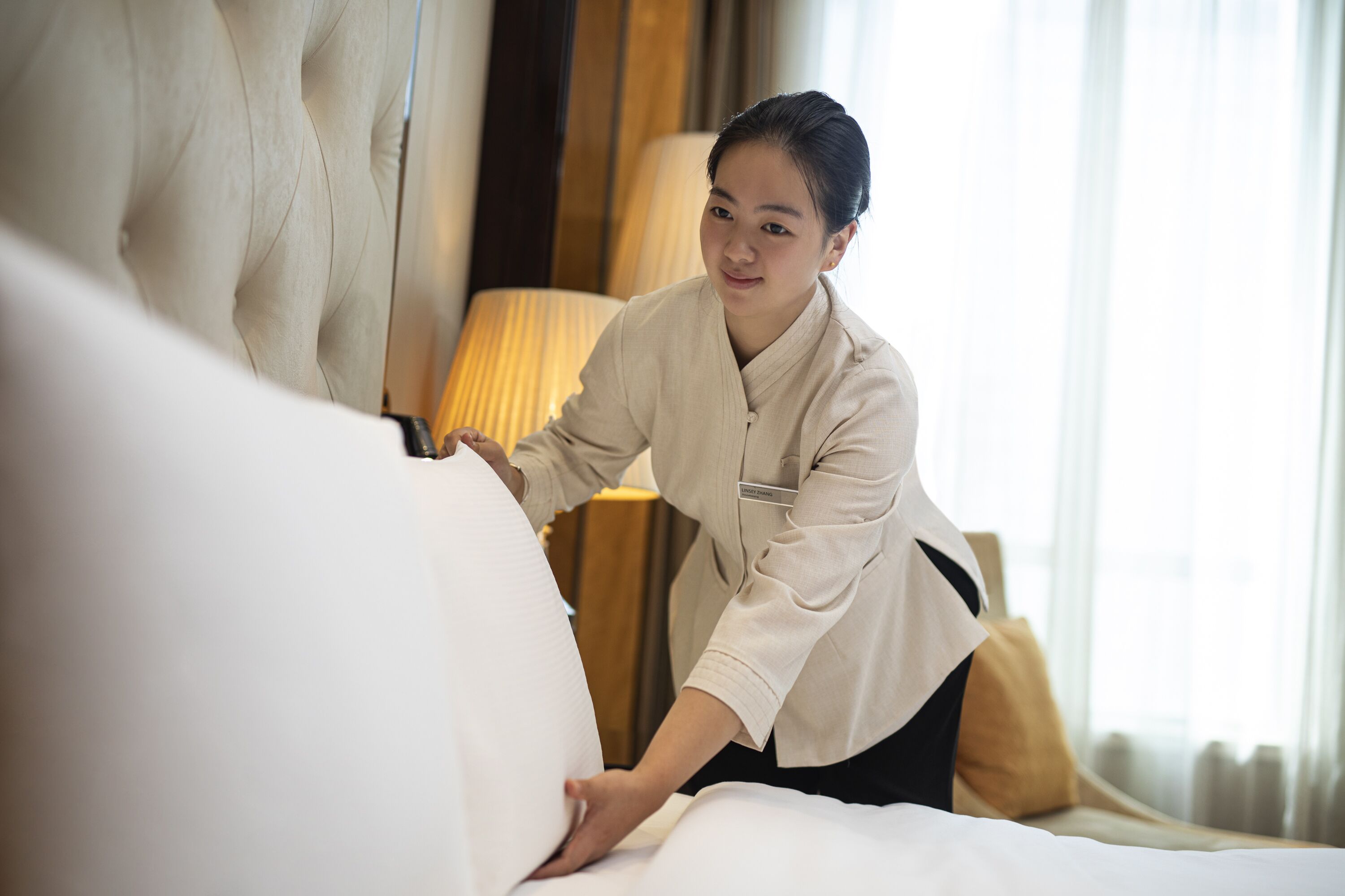 A hotel room with a large bed, a bedside lamp, and a view of the outdoors through the window.
