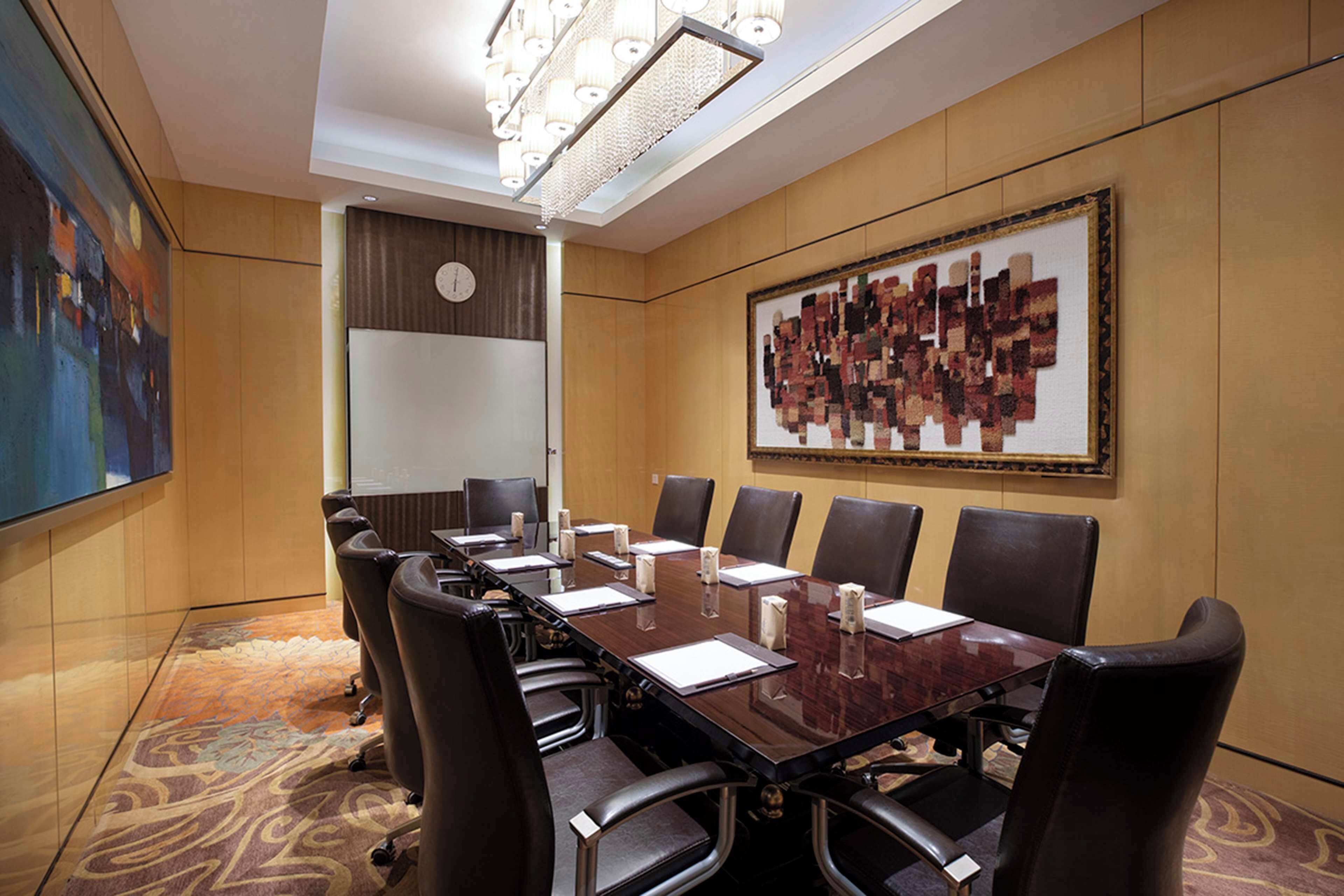 Une salle de conférence avec une longue table, de nombreuses chaises, une horloge au mur et un grand tableau abstrait.