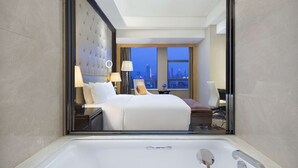 A hotel room with a large bed, a sitting area, a view of the cityscape, and a bathtub. - Hilton Nanjing (Nanjing)