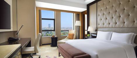 A hotel room with a large bed, a desk, a chair, a TV, and a view of the city.