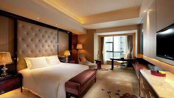 A hotel room with a large bed, a desk, a TV, a chair, and a lamp.