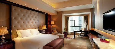 A hotel room with a large bed, a desk, a TV, a chair, and a lamp.