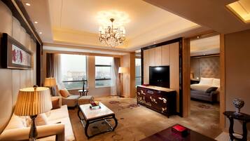 A spacious hotel room with a large bed, a TV, a sofa, a coffee table, and a view of the city.