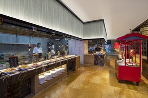 A buffet area with a marble counter, multiple food stations, and a red food cart. - Hilton Nanjing (Nanjing)