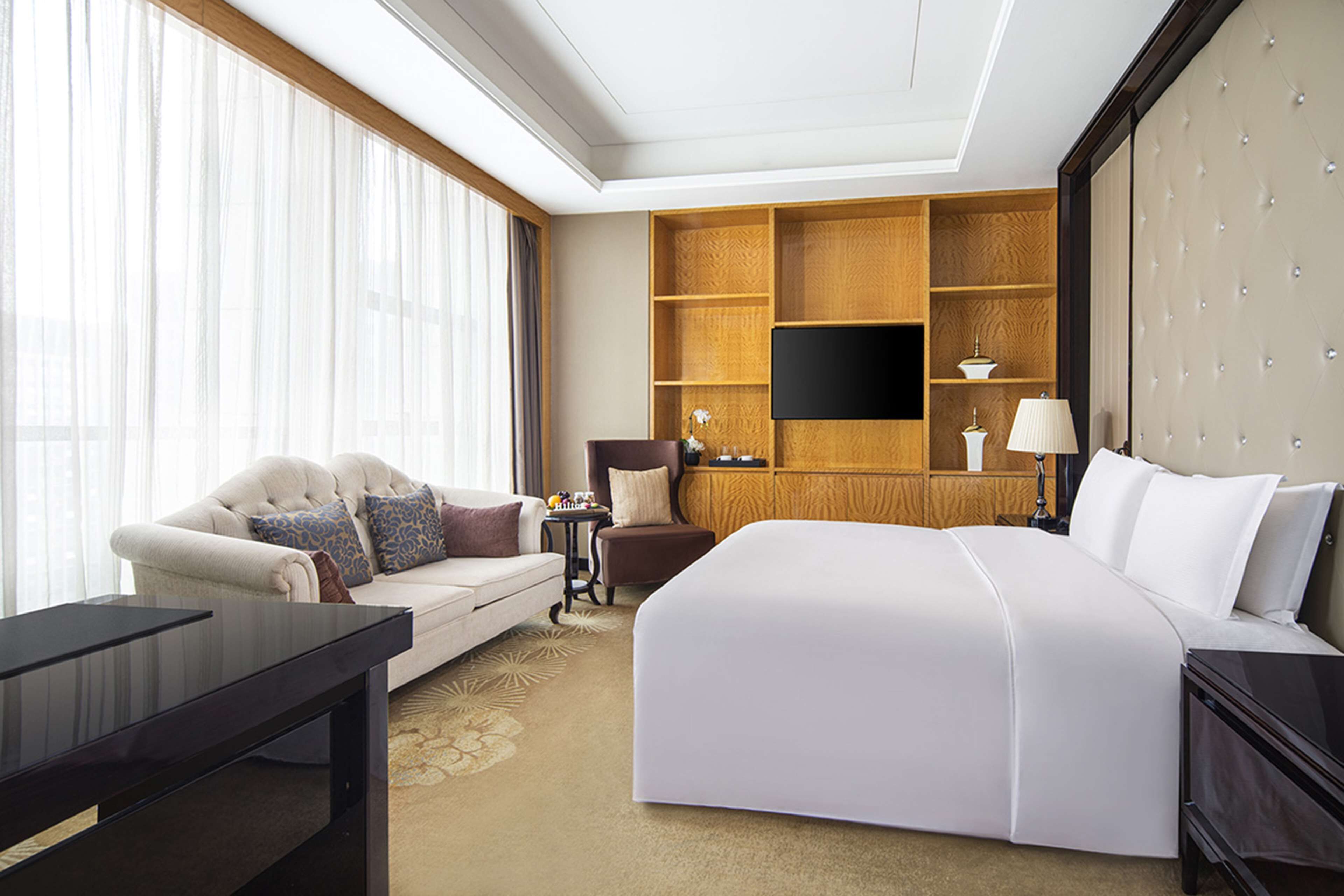 Une chambre d’hôtel avec un grand lit, un canapé, un bureau, une télévision et un mur recouvert de panneaux en bois.