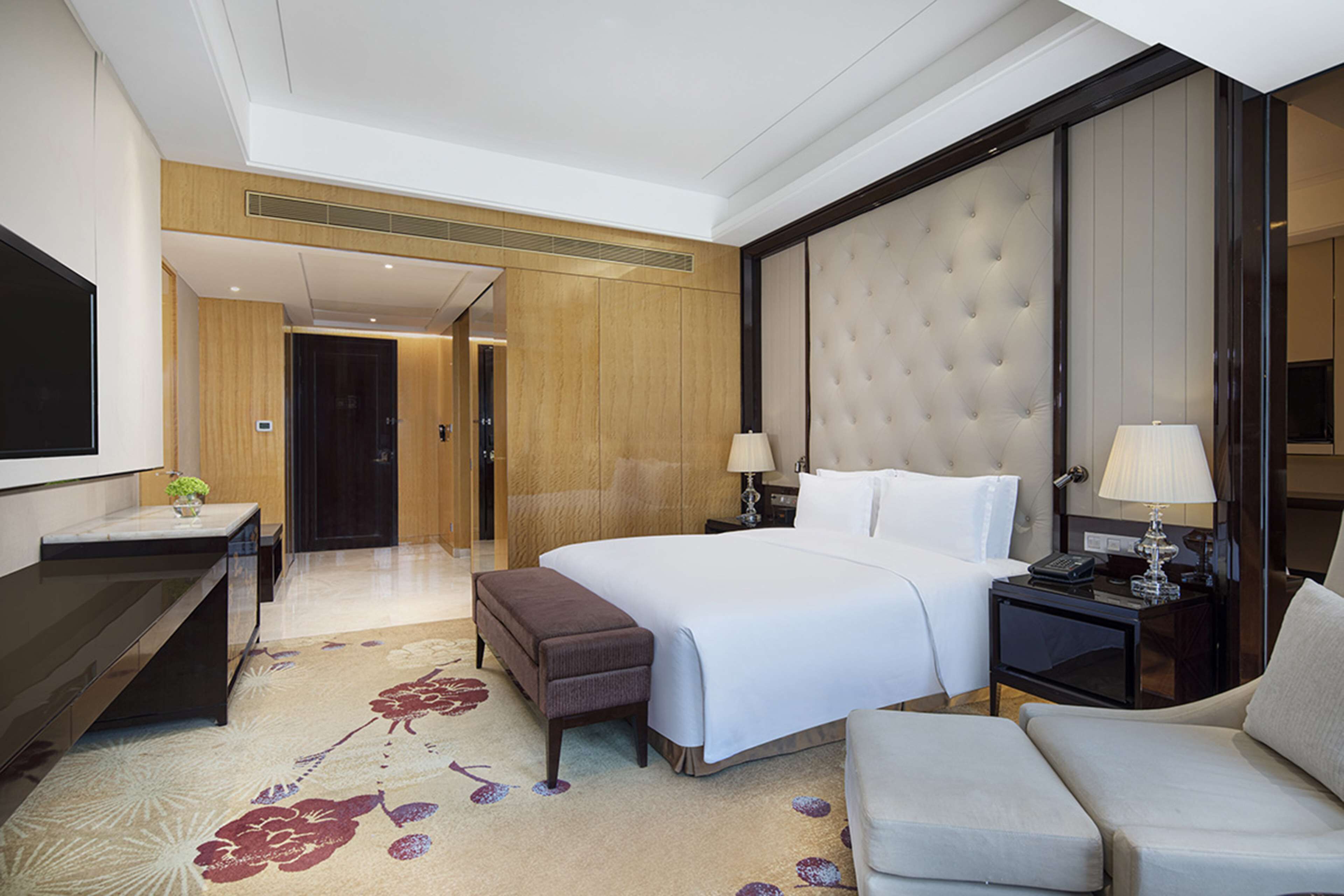 A hotel room with a large bed, a desk with a computer, a seating area, and a television.