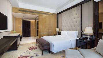 A hotel room with a large bed, a desk with a computer, a seating area, and a television.