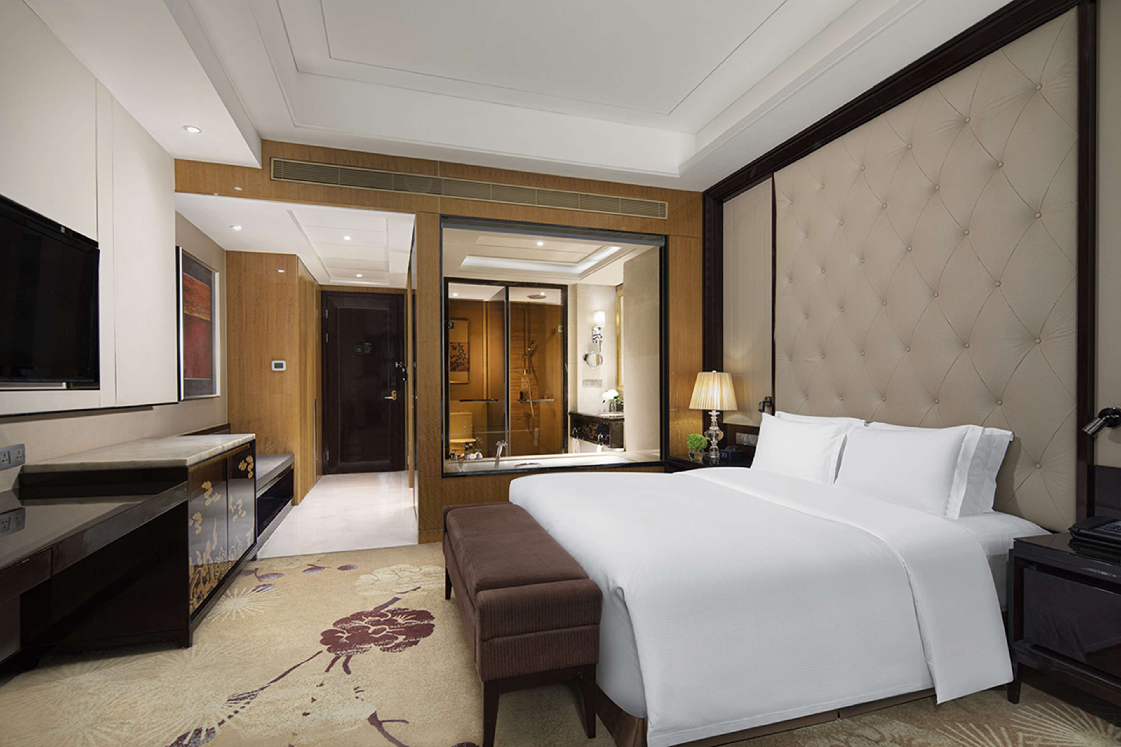 A hotel room with a large bed, a desk, a TV, and a bathroom visible through an open door.
