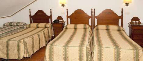 A room with three wooden beds, each with a patterned bedspread and a nightstand with a lamp.