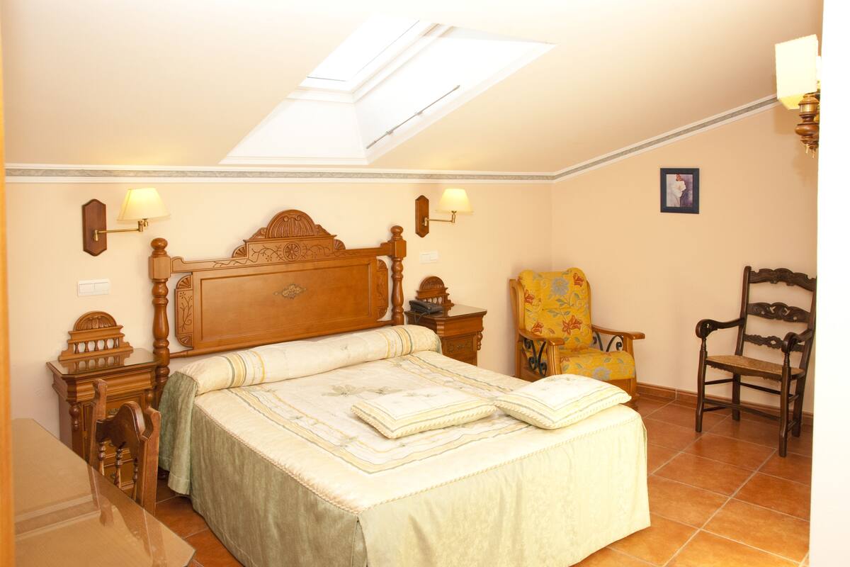 A bedroom with a wooden bed, two bedside lamps, a chair, and a small table.